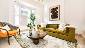 Een woonkamer met een groene bank, een oranje fauteuil en een ronde salontafel met een fles en glazen.