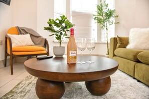Ein runder Couchtisch aus Holz mit einer Flasche, zwei Gläsern, einer Fernbedienung und einem Blumentopf darauf.