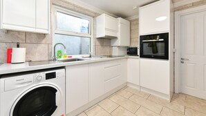 Een moderne keuken met witte kasten, een ingebouwde wasmachine, een magnetron en een raam met uitzicht.
