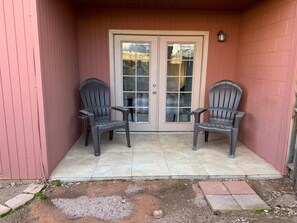 Ein überdachter Patio-Bereich mit zwei Adirondack-Stühlen, einer Schiebetür und einer kleinen Wandleuchte.