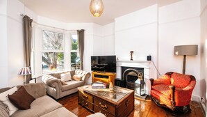Un salon comprenant un canapé, un fauteuil rouge, une table basse en bois, un téléviseur et une cheminée.