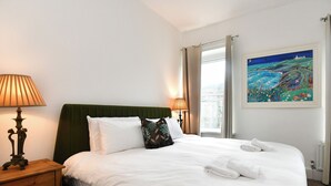 Un lit bien fait, avec du linge de lit blanc et deux oreillers, une table de chevet avec une lampe et un tableau accroché au mur.