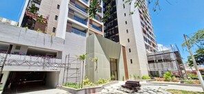A multi-story building with a modern architectural design, featuring a mix of glass and concrete facades, and a landscaped courtyard with plants and a seating area. - COARM0111 - Condominio LIT 760 (Salvador)