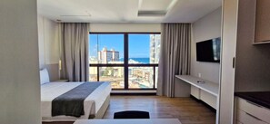 A hotel room with a bed, a TV, a desk, and a balcony with a city view. - COARM0111 - Condominio LIT 760 (Salvador)