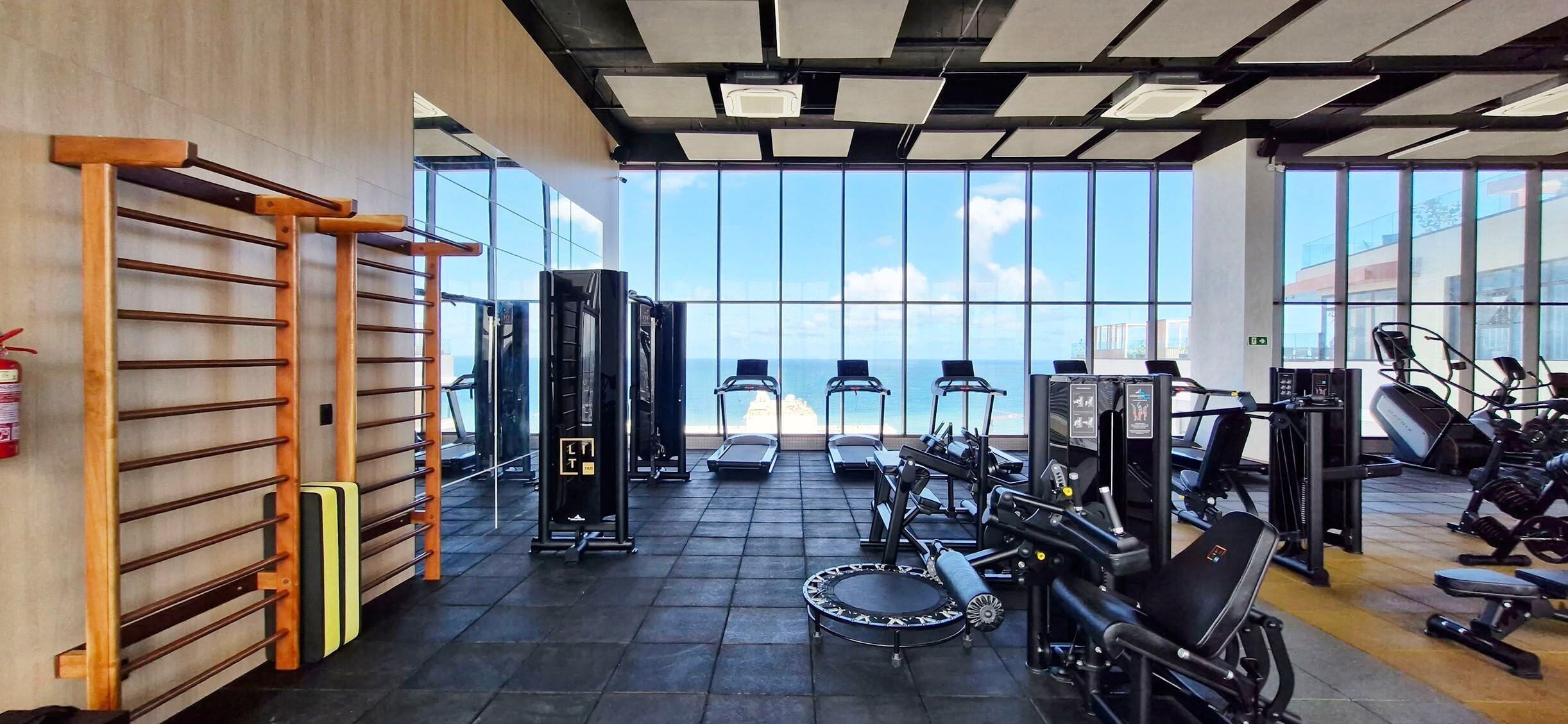 A gym with exercise equipment, a pull-up bar, and large windows overlooking a body of water.