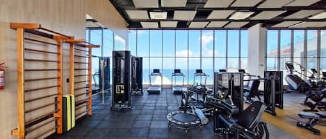 A gym with exercise equipment, a pull-up bar, and large windows overlooking a body of water.