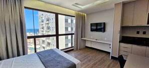 A hotel room with a large window, a bed, a TV, and a kitchenette. - COARM0111 - Condominio LIT 760 (Salvador)