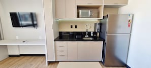 Eine kleine Küche mit Flachbildfernseher, Mikrowelle, Kaffeemaschine, Kühlschrank und Spüle.