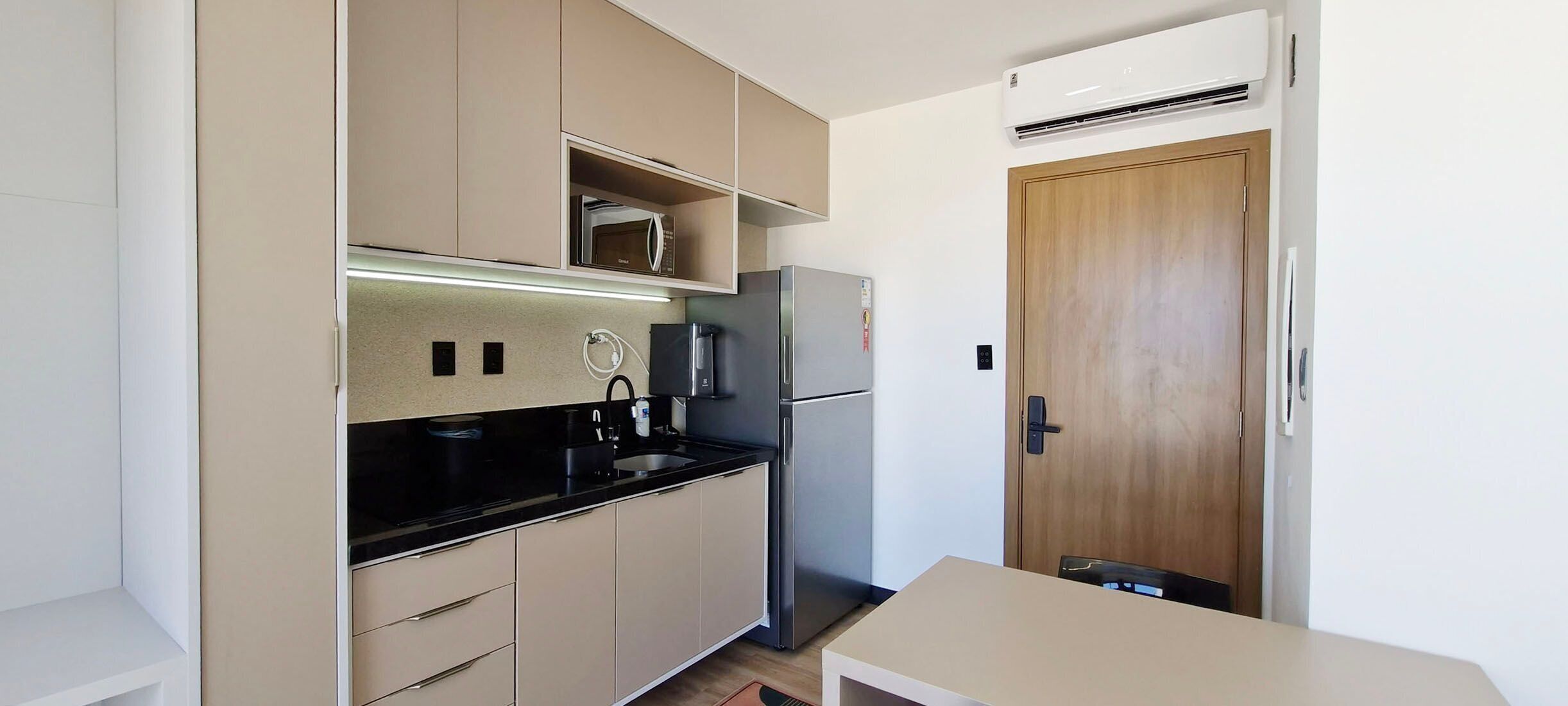 A compact kitchen with a microwave, refrigerator, and a wooden door.