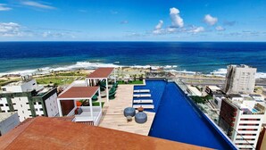 Piscina no terraço com vista para o oceano, cercada por edifícios e um céu claro.