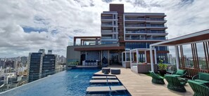 A rooftop pool with lounge chairs and a modern building in the background. - COARM0111 - Condominio LIT 760 (Salvador)