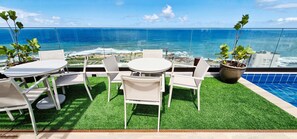 A balcony with a view of the ocean, a round table, white chairs, and potted plants. - COARM0111 - Condominio LIT 760 (Salvador)