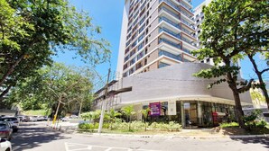 Um edifício moderno com fachada curva, rodeado por árvores e um estacionamento.