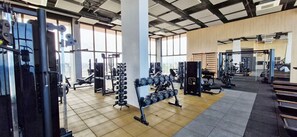 Een sportschool met diverse fitnessapparaten, grote ramen en een betegelde vloer.
