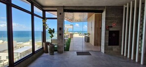 Eine moderne Hotelhalle mit großen Fenstern, Topfpflanzen und Blick aufs Meer.
