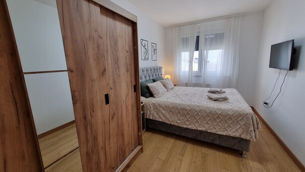 A bedroom with a bed, a wardrobe, a television, and artwork on the wall. - Dea Lux Family Apartment (Novi Sad)