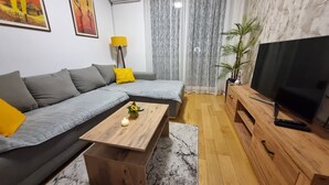 A modern living room with a grey sectional sofa, a wooden coffee table, a TV on a wooden stand, and a potted plant. - Dea Lux Family Apartment (Novi Sad)