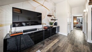 A modern living room with a large flat-screen TV, a black entertainment unit, and a decorative wall with leaf patterns. - The Lantern Loft | Luxury Riverfront Downtown (Wilmington)
