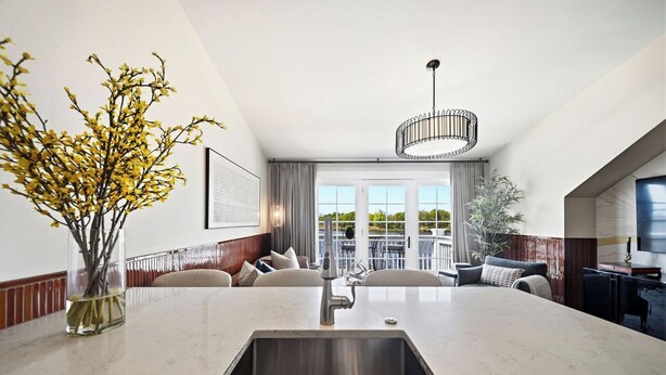 A modern kitchen with a central island, a dining area with a sofa, and a view of the outdoors through large windows. - The Lantern Loft | Luxury Riverfront Downtown (Wilmington)