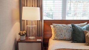 A neatly made bed with patterned pillows, a bedside lamp, and a small vase with flowers on a wooden nightstand. - The Lantern Loft | Luxury Riverfront Downtown (Wilmington)