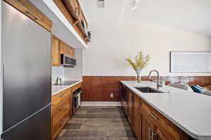 A modern kitchen with wooden cabinets, stainless steel appliances, a herringbone-patterned backsplash, and a large island with a sink. - The Lantern Loft | Luxury Riverfront Downtown (Wilmington)