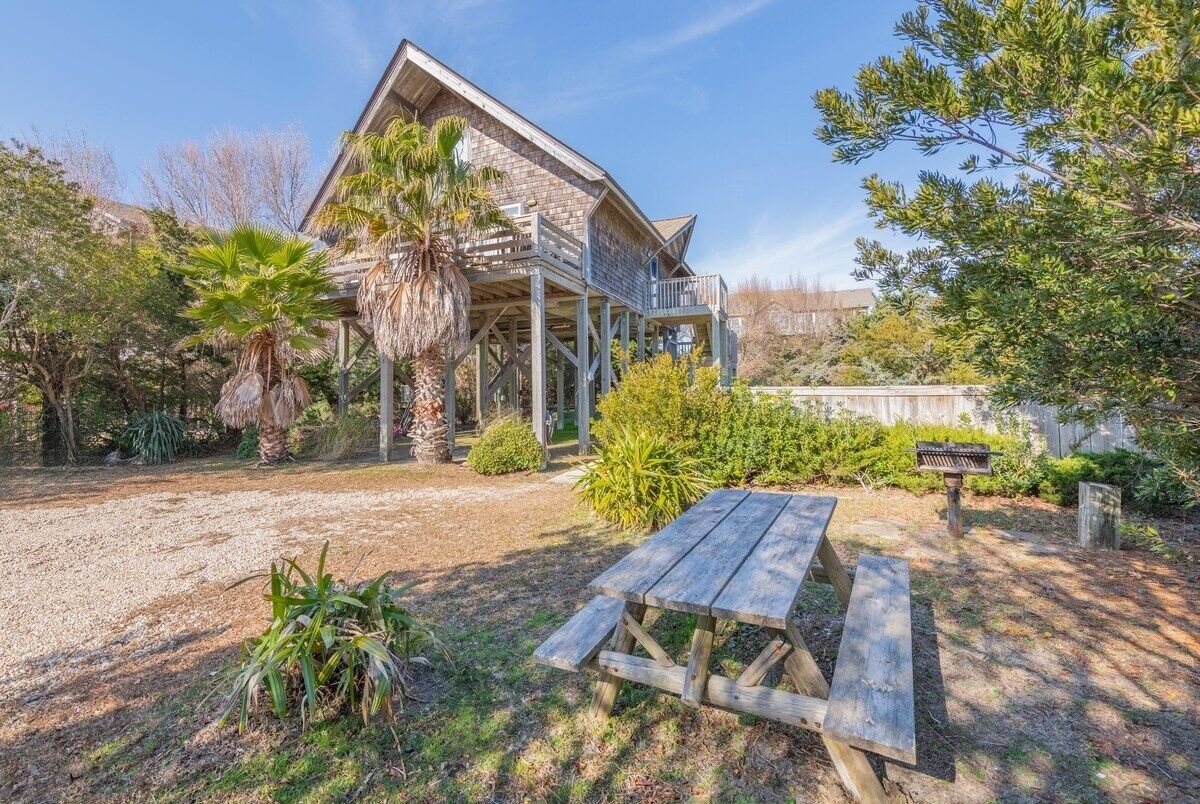 Une maison en bois dotée d’un balcon, entourée de différentes plantes et agrémentée d’une table de pique-nique.
