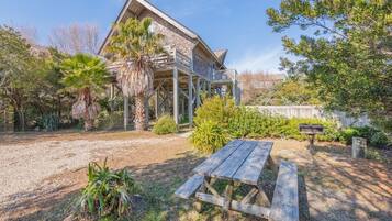 Une maison en bois dotée d’un balcon, entourée de différentes plantes et agrémentée d’une table de pique-nique.