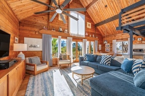 A cozy log cabin interior with a high ceiling, wooden beams, a large ceiling fan, a sofa set, a dining area, and a kitchen. - The Stoke - 5 houses to Ocean - Pool! (Salvo)
