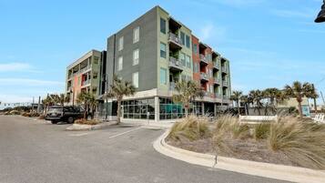 A multi-story building with balconies, a parking lot, and palm trees.