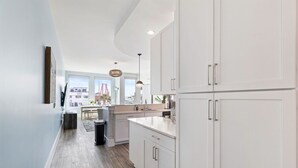 Une cuisine moderne avec des meubles blancs, un plancher en bois et une vue sur le paysage urbain, visible à travers de grandes fenêtres.