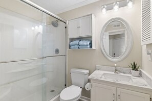 Une salle de bain dotée d’une douche à parois de verre, de toilettes, d’un lavabo avec un plan de travail en marbre et d’un meuble-lavabo avec des placards.