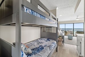 Une chambre avec des lits superposés offrant une vue sur l’océan, un balcon et un coin cuisine moderne.