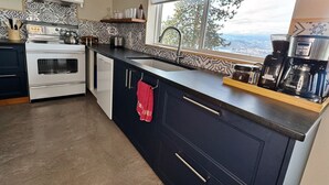 A modern kitchen with a large island, a stove, a sink, and a coffee maker. - Stone & Vines | 2BR Wine Country Retreat | Adventure by Day, Wine by Night (Naramata)