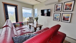 A living room with a red leather sofa, a television mounted on the wall, and framed pictures depicting outdoor scenes. - Stone & Vines | 2BR Wine Country Retreat | Adventure by Day, Wine by Night (Naramata)