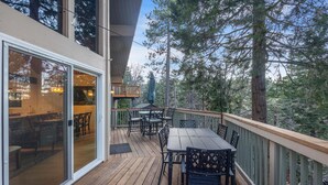 Eine Holzterrasse mit Tisch und Stühlen, eine Glastür, die zu einem Innenbereich führt, und Blick auf Bäume.