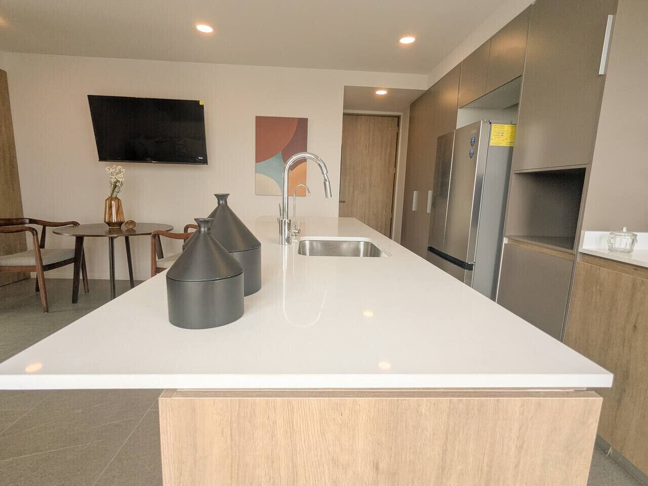 A modern kitchen with a large island, stainless steel appliances, and a flat-screen TV mounted on the wall.