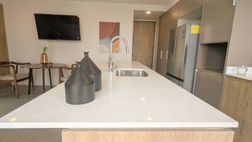 A modern kitchen with a large island, stainless steel appliances, and a flat-screen TV mounted on the wall.