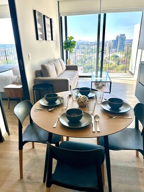 Zona pranzo moderna con tavolo rotondo per quattro persone, divano e balcone con vista sulla città.
