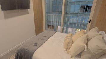 Un dormitorio con cama, almohadas, televisor y ventana con vista al exterior.