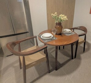 Un comedor con una mesa redonda de madera, cuatro sillas de madera, un florero con flores y un vaso de agua.