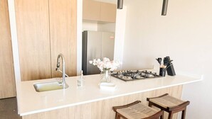 Une cuisine moderne avec un plan de travail blanc, des appareils en acier inoxydable et des tabourets de bar en bois.