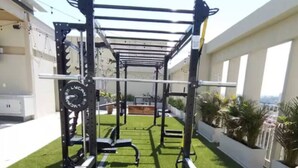 Un espace de remise en forme en plein air équipé d’une barre de traction, d’un banc de musculation et d’élastiques de résistance, le tout installé sur une surface de gazon synthétique.