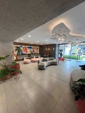 A spacious living area with a curved grey sofa, pink poufs, and a colorful abstract mural on the wall. - Departamento de Lujo en La Paz – Torre Neoliving (Guadalajara)