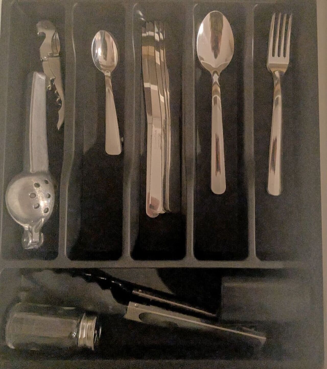 A set of silverware including a spoon, fork, knife, and a small bowl, all placed in a black tray.