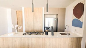 Une cuisine moderne dotée d’un îlot central, d’appareils électroménagers en acier inoxydable et de luminaires suspendus.