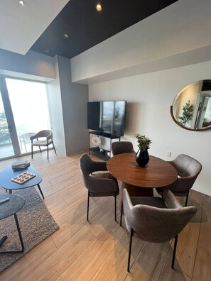 A modern living room with a round wooden dining table, six chairs, a flat-screen TV, a large mirror, and a view of the outdoors through a large window. - Moderno Dpt Nuevo Lobby 33 Zona Exclusiva Andares (Zapopan)