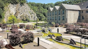 Um edifício de pedra com estilo arquitetônico tradicional, rodeado por um jardim paisagístico com lago e caminhos.