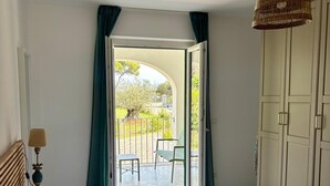 A hotel room with a bed, a lamp, a wardrobe, and a view of an outdoor patio. - Two Bedroom Apartment with Garden View (Portoferraio)