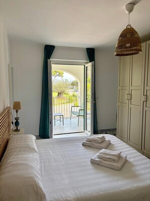 A hotel room with a bed, a lamp, a wardrobe, and a view of an outdoor patio. - Two Bedroom Apartment with Garden View (Portoferraio)