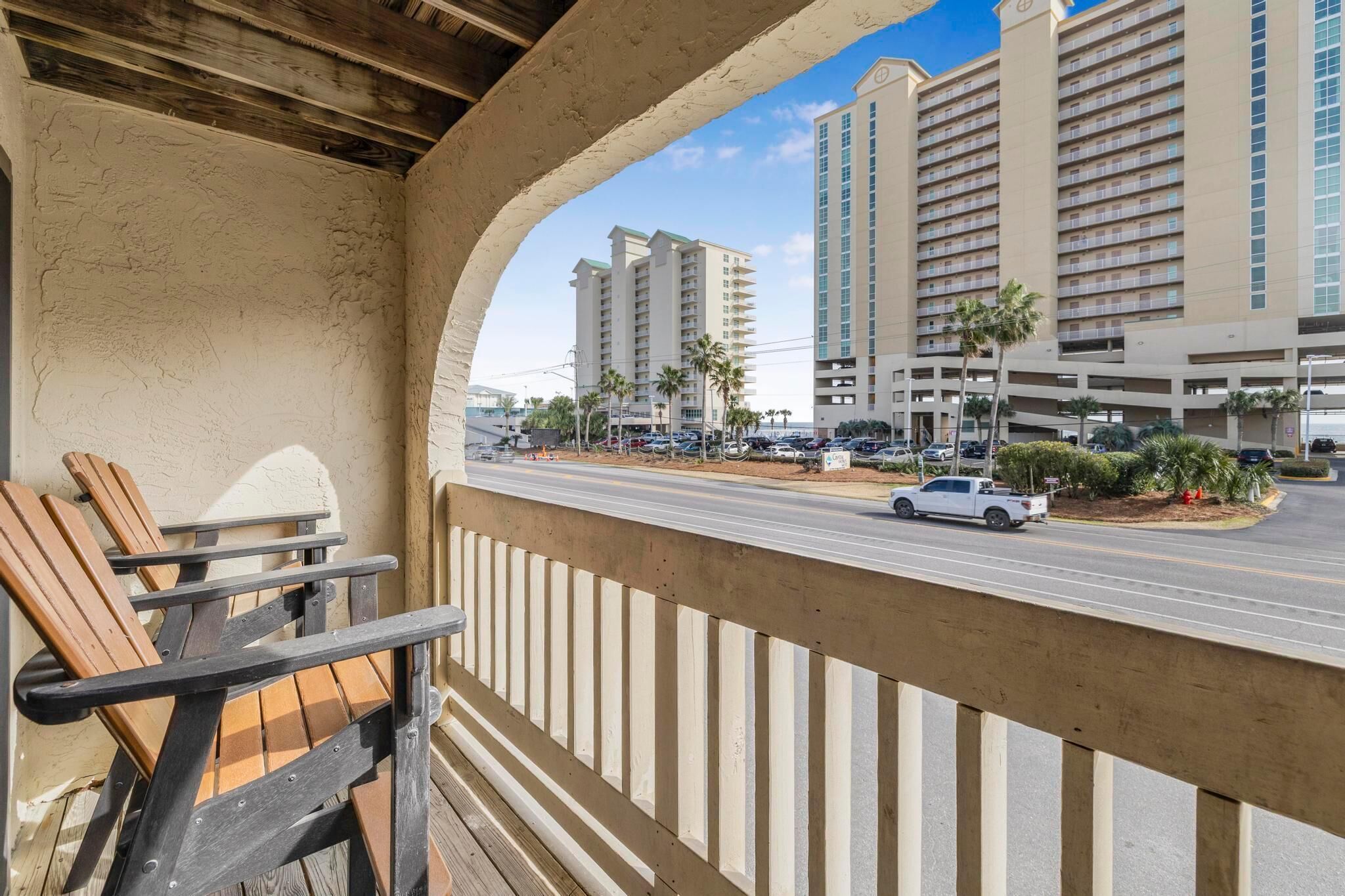 A balcony with wooden chairs, overlooking a street with cars and tall buildings.